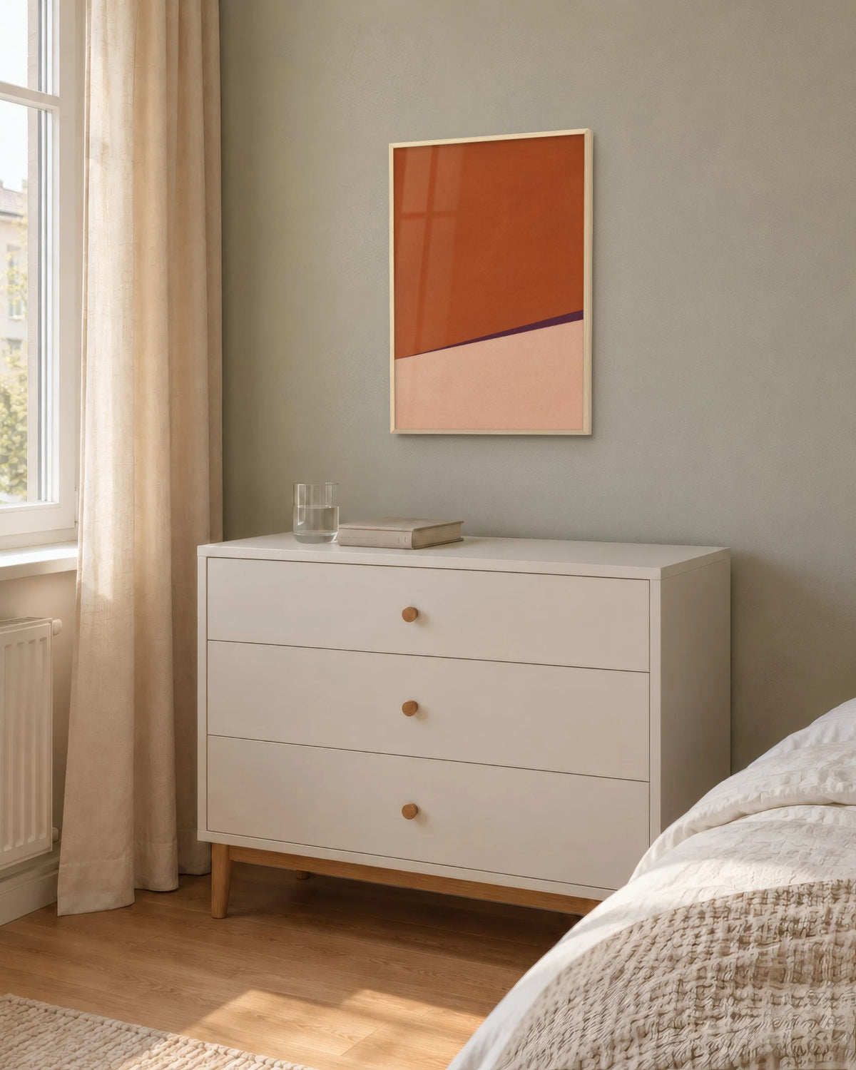 Affiche chambre minimaliste terracotta en cadre chêne clair sur un mur sauge, au-dessus d'une commode blanche
