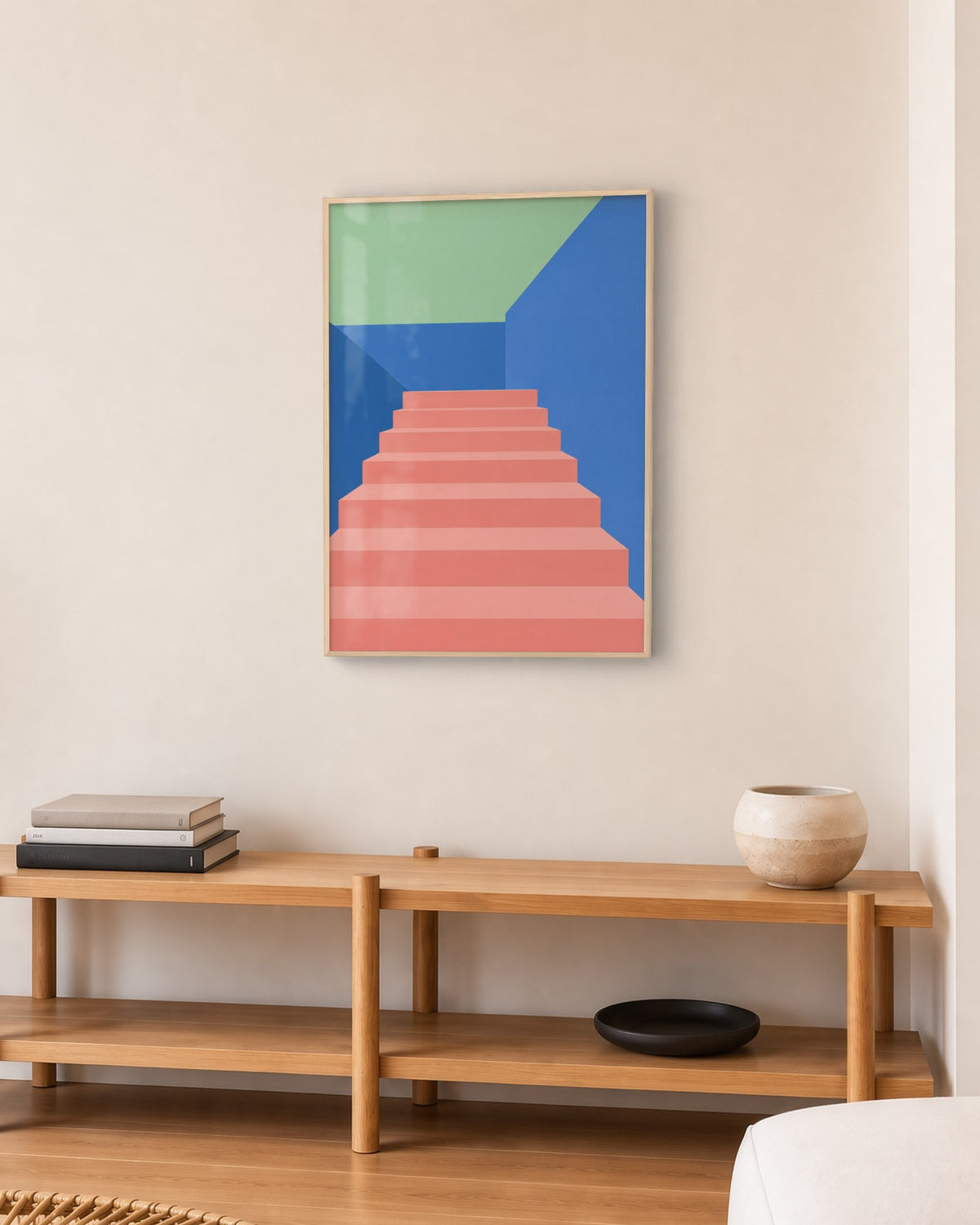 Affiche escalier rose et murs bleus en cadre chêne clair au-dessus d’un meuble bas en chêne et rotin