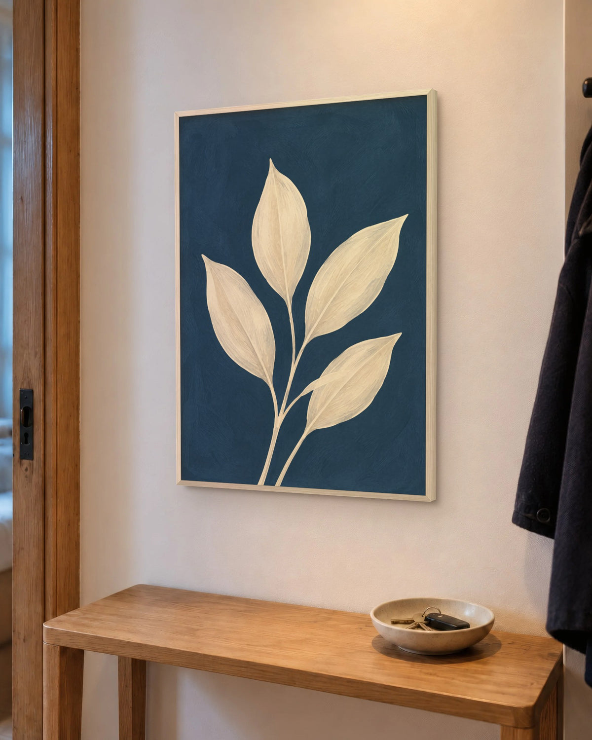 Affiche entrée feuilles crème sur bleu nuit en cadre chêne clair au-dessus d'une console en chêne