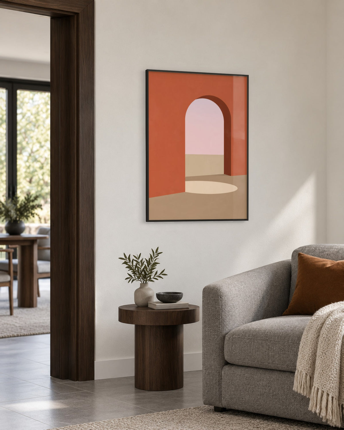 Affiche arche terracotta ouvrant sur un ciel rose, cadre noir, salon au fauteuil gris et guéridon noyer