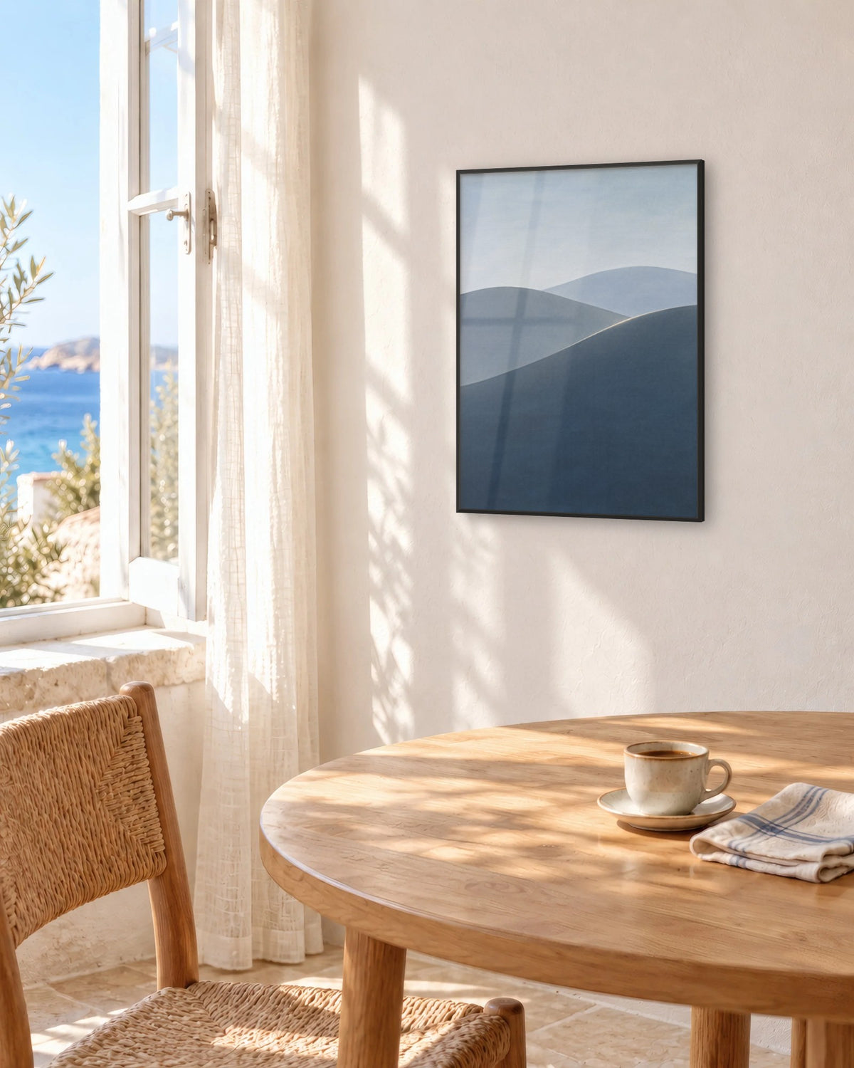 Affiche salle à manger paysage bleu gris encadrée en noir au-dessus d'une table ronde face à la mer