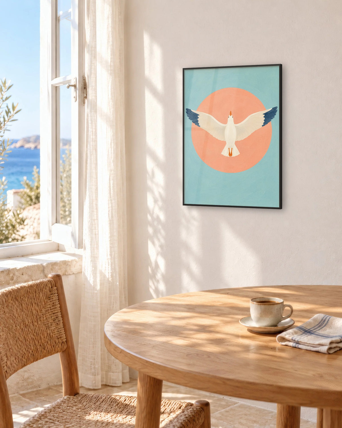 Affiche bord de mer bleu et rose encadrée en noir au-dessus d'une table ronde face à la mer