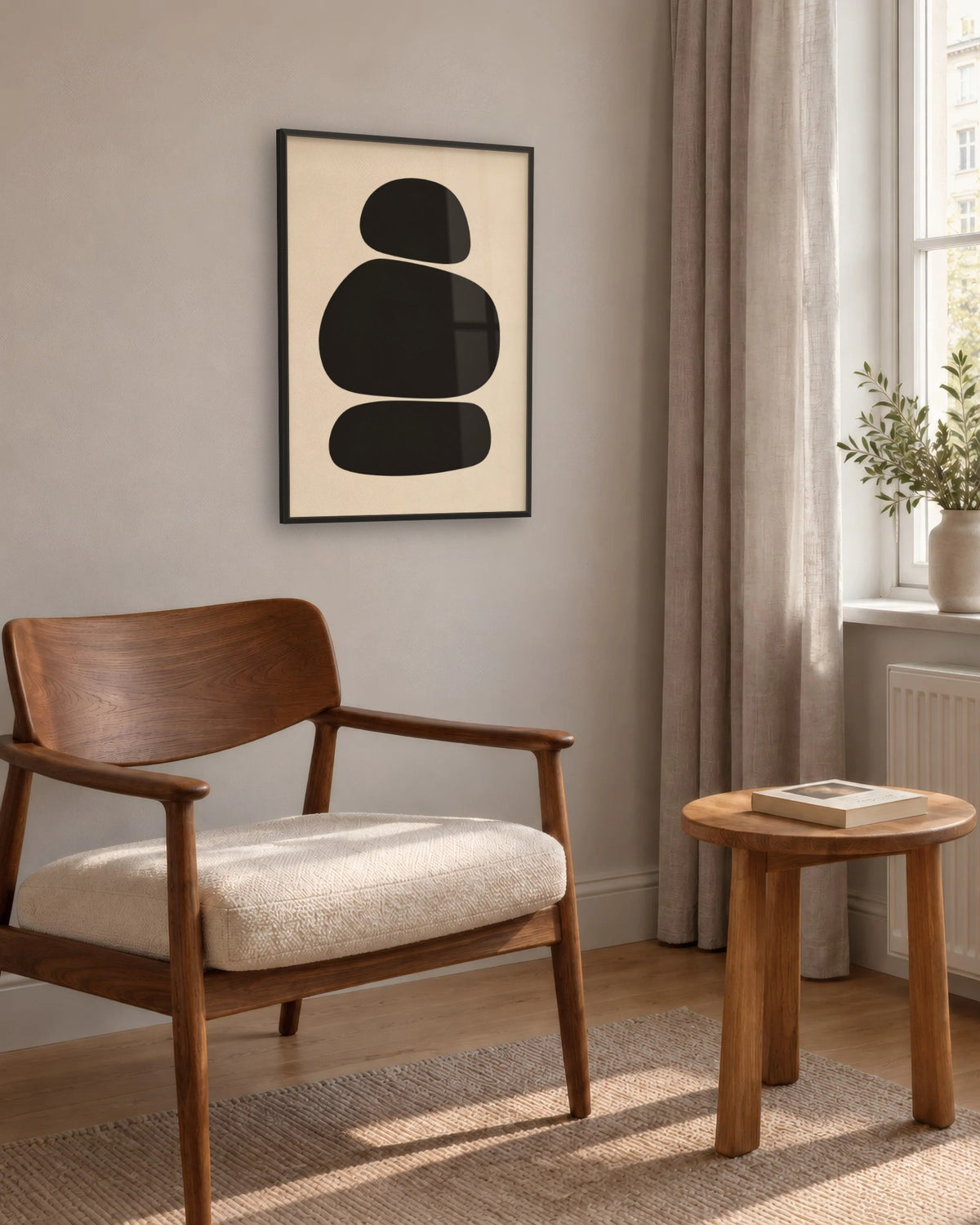 Affiche galets noirs minimaliste encadrée en noir près d'un fauteuil en noyer et d'un tabouret