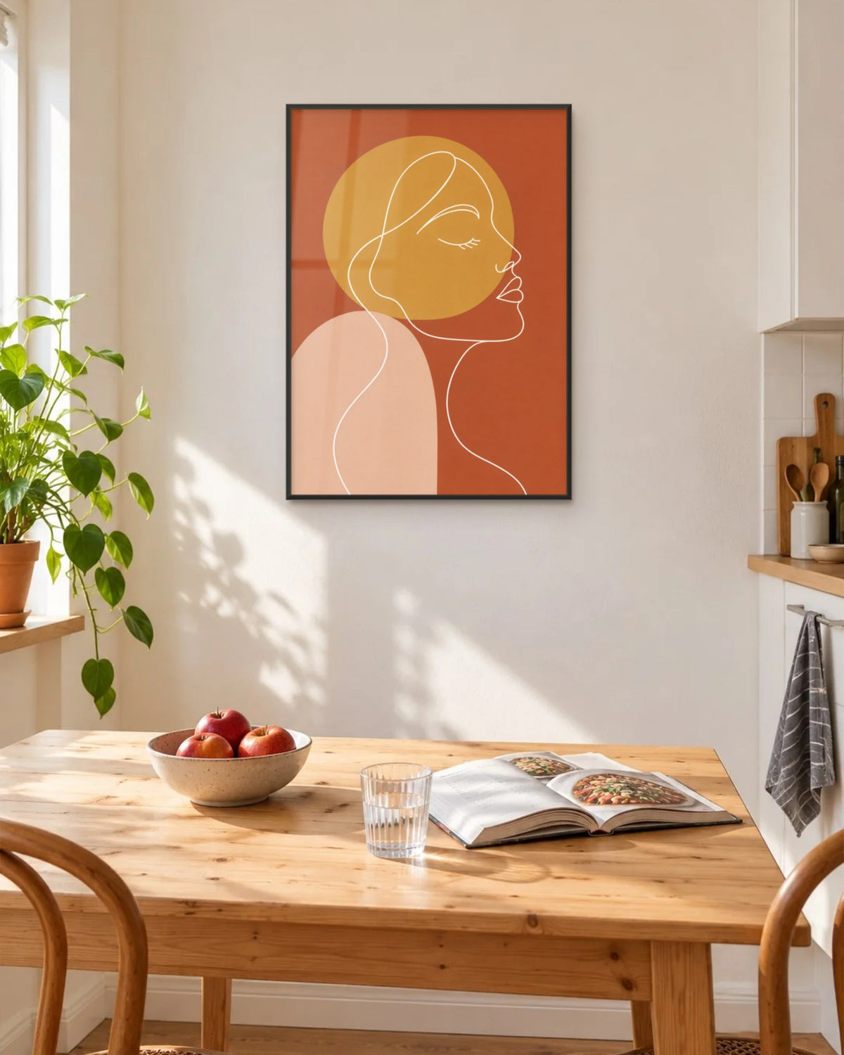 Affiche cuisine visage au trait blanc encadrée en noir sur un mur crème, au-dessus d'une table en pin