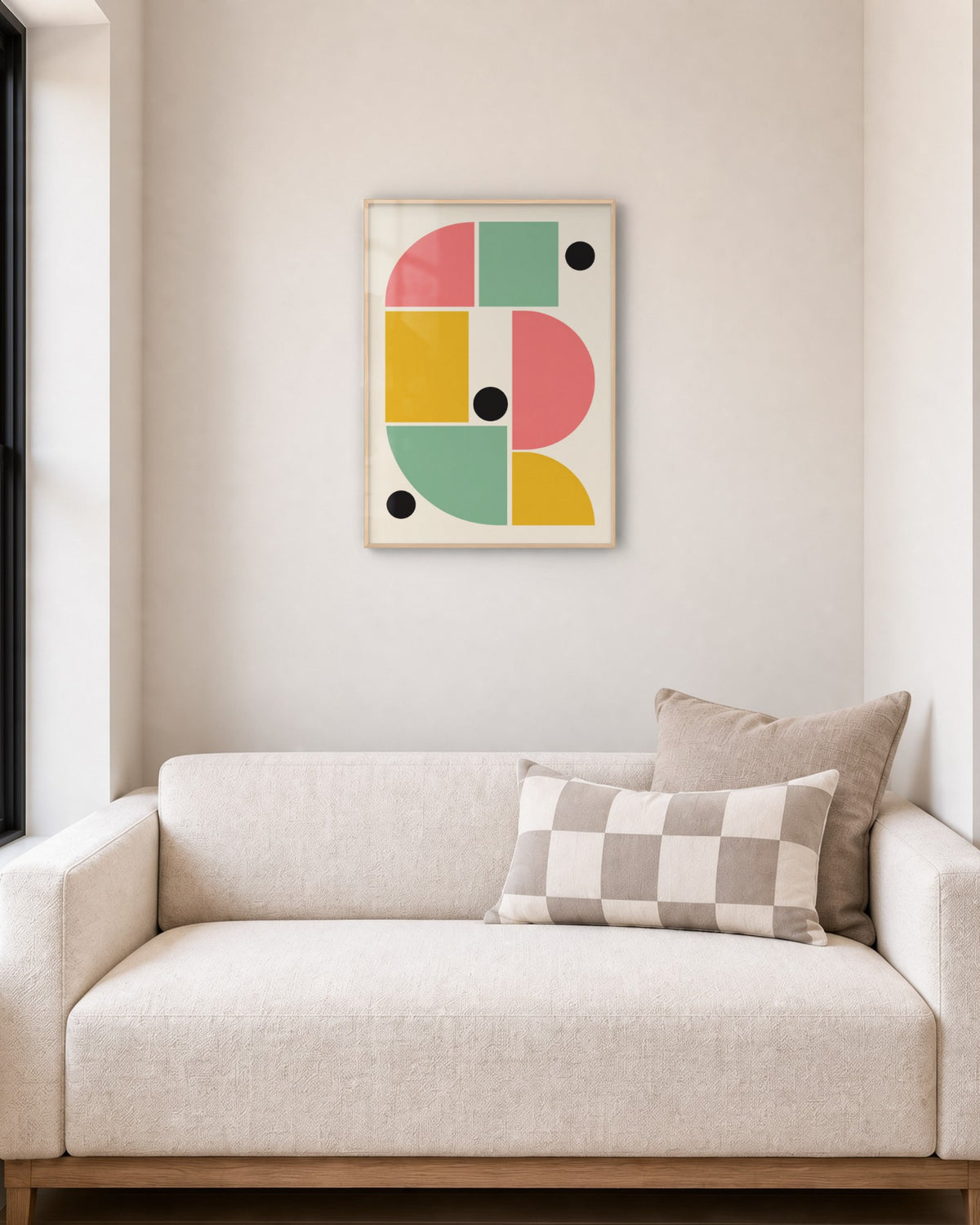Affiche géométrique Bauhaus rose, jaune et vert en cadre chêne clair au-dessus d’un petit canapé écru