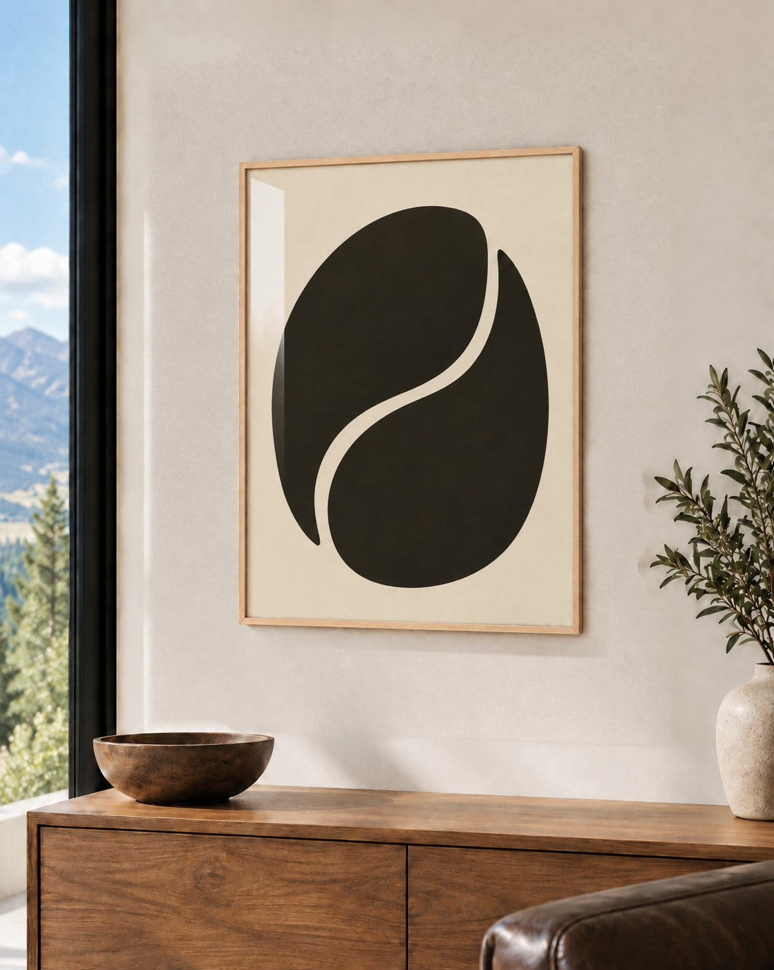 Affiche minimaliste forme noire ovale traversée d’une courbe crème, cadre en bois naturel au-dessus d’un buffet en noyer face à la montagne