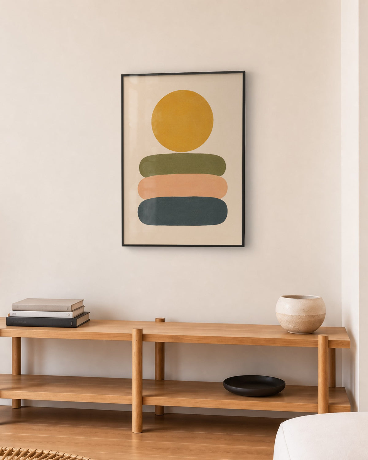 Affiche soleil ocre sur galets olive, pêche et bleu nuit empilés, cadre noir, au-dessus d’un meuble en chêne