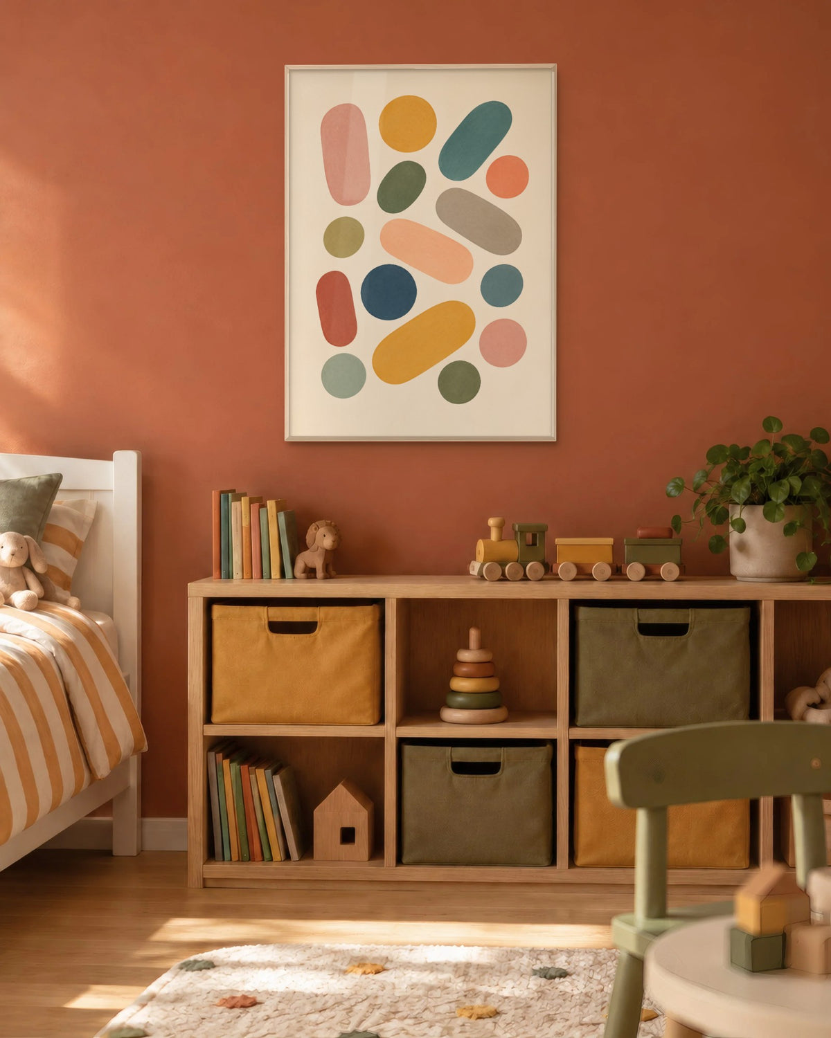 Affiche chambre d'enfant formes colorées en cadre chêne clair sur un mur terracotta, près d'une étagère