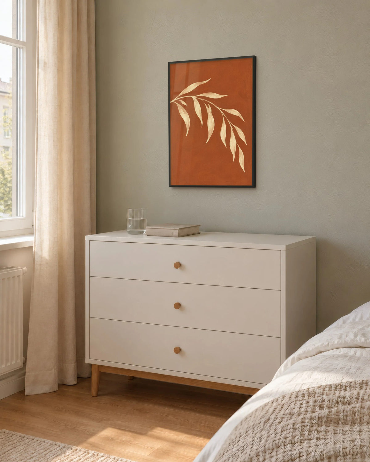 Affiche chambre botanique terracotta encadrée en noir sur un mur sauge, au-dessus d'une commode